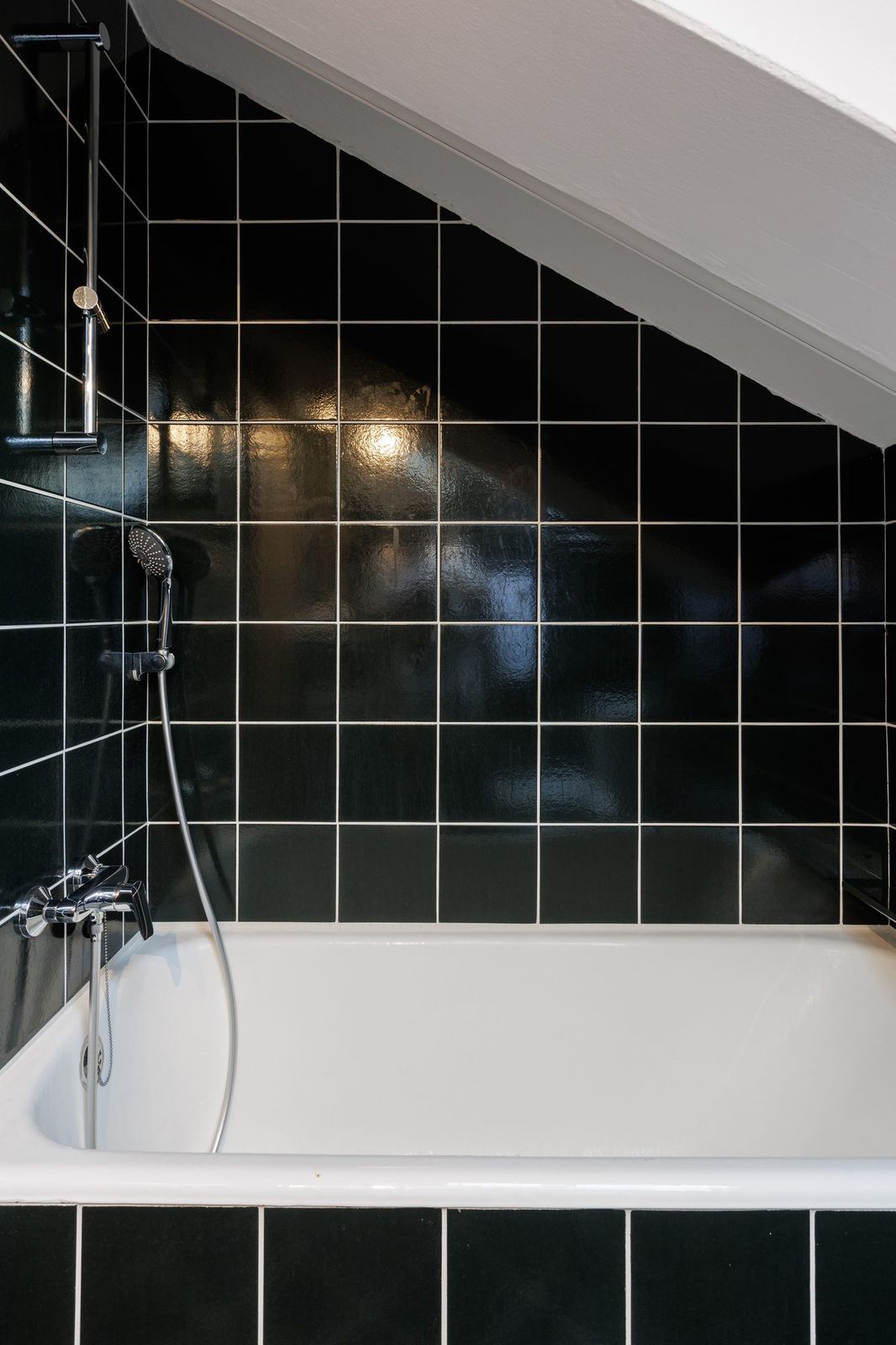 Attic bathroom, detail of the bathtub with hand shower and black tiles