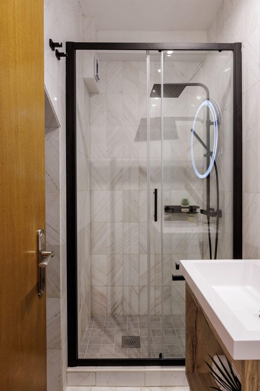 Modern bathroom with glass shower enclosure and light marble-effect tiles